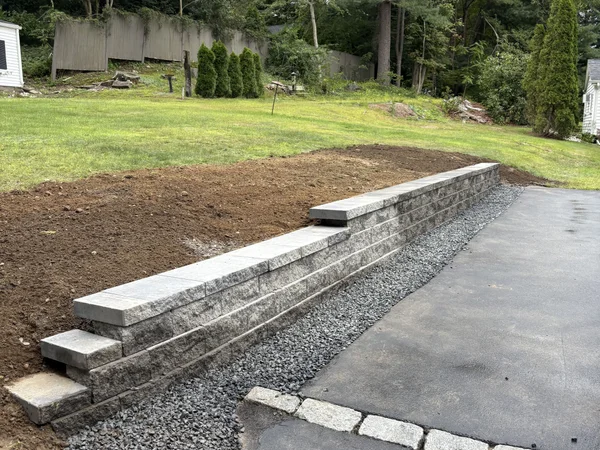 Block retaining wall with cap stones along driveway by MAC Excavation & Landscape in South Shore MA
