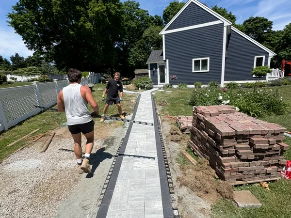 MAC crew installing a porcelain paver walkway with charcoal border in a Scituate, MA backyard