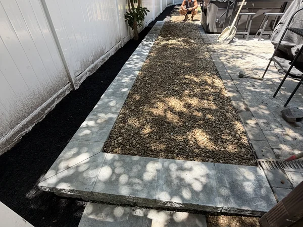 MAC crew installing a river rock drainage walkway with paver border along a fence line in Marshfield, MA