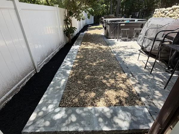 Finished river rock walkway with concrete paver border beside a hot tub patio in Marshfield, MA