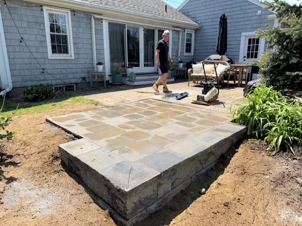 Raised paver patio under construction behind a home in Plymouth, MA